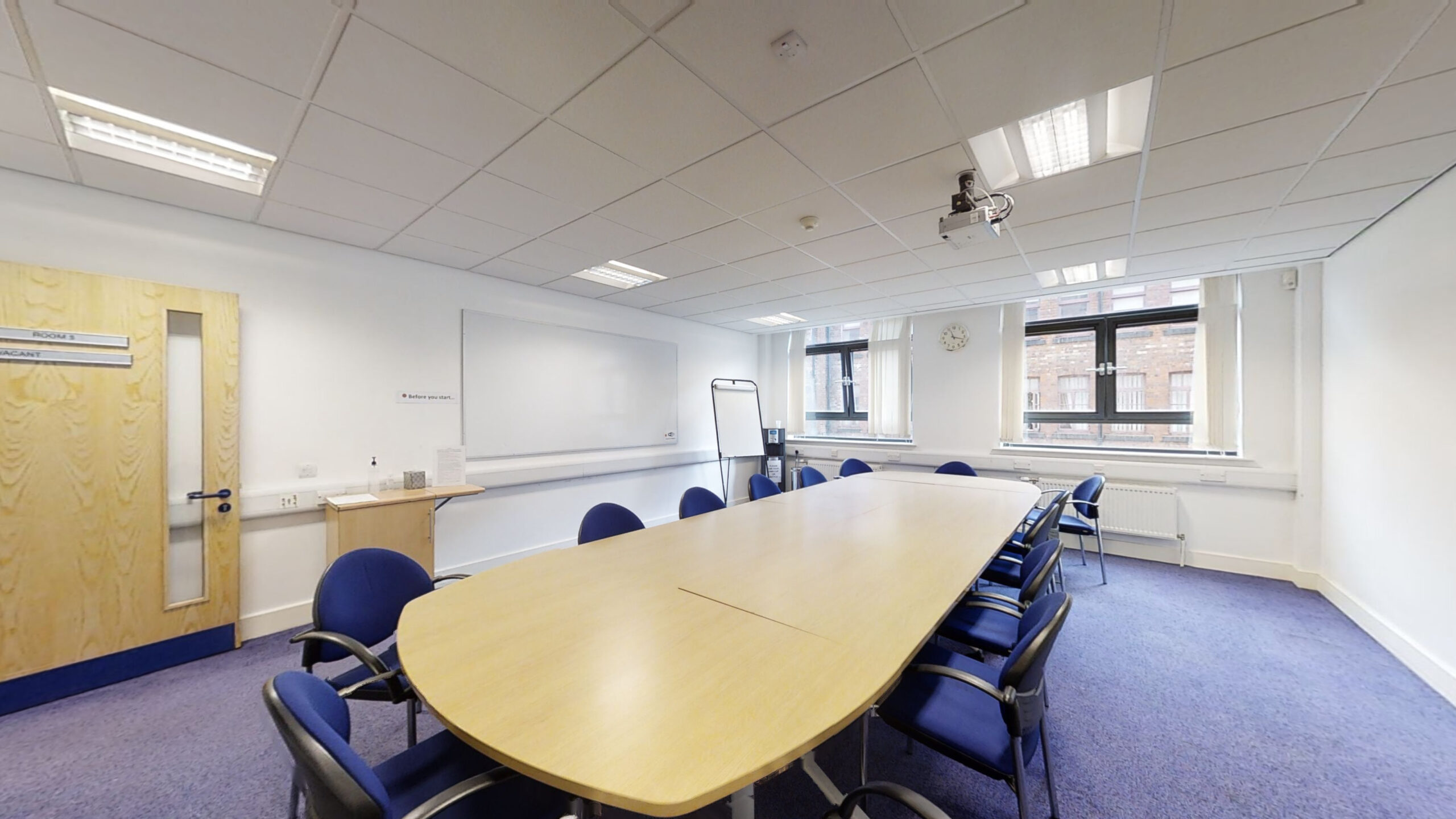 A spacious conference room featuring blue chairs arranged around a whiteboard.