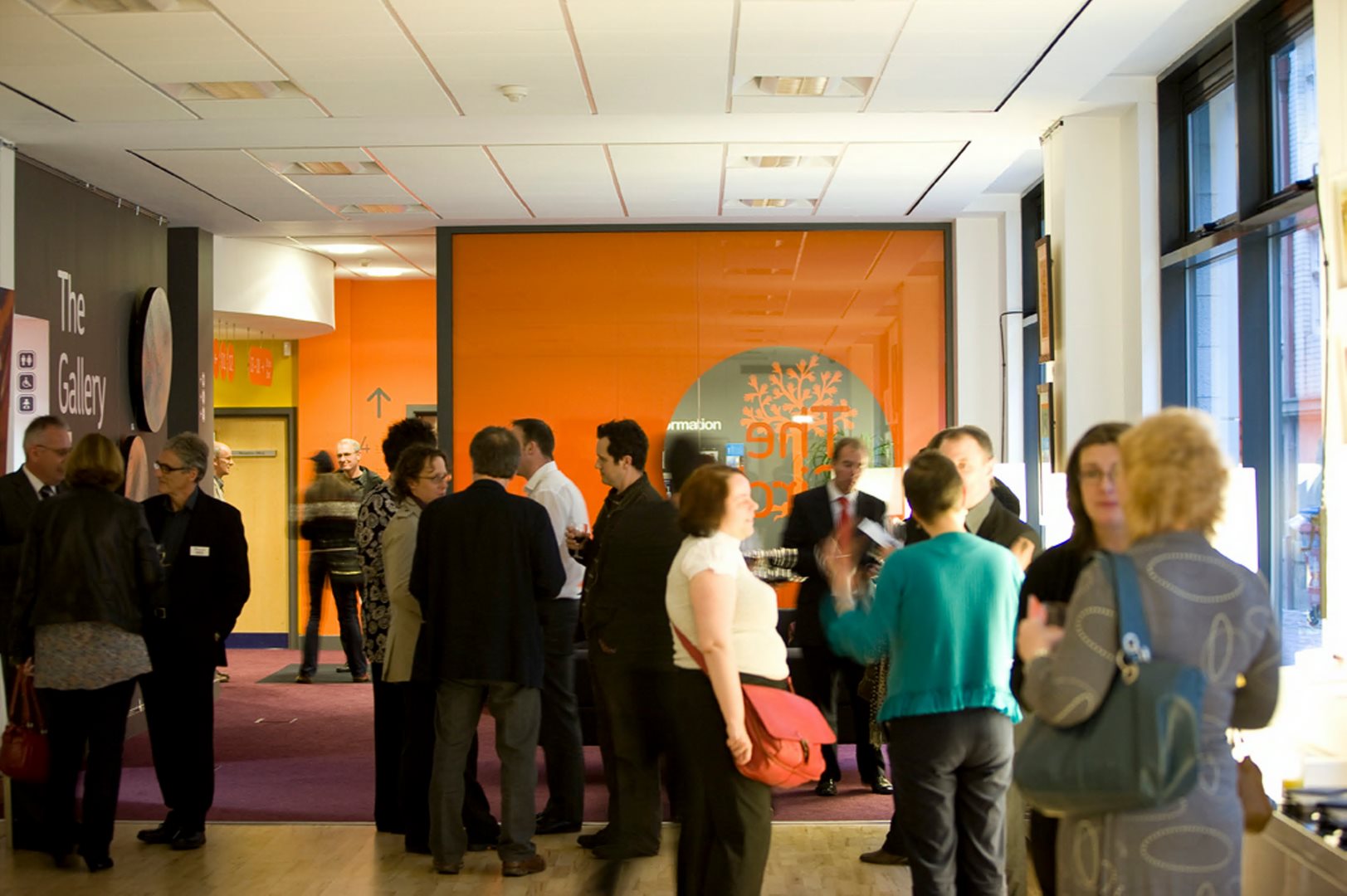 A group of diverse individuals standing together in a well-lit hallway, engaged in conversation.