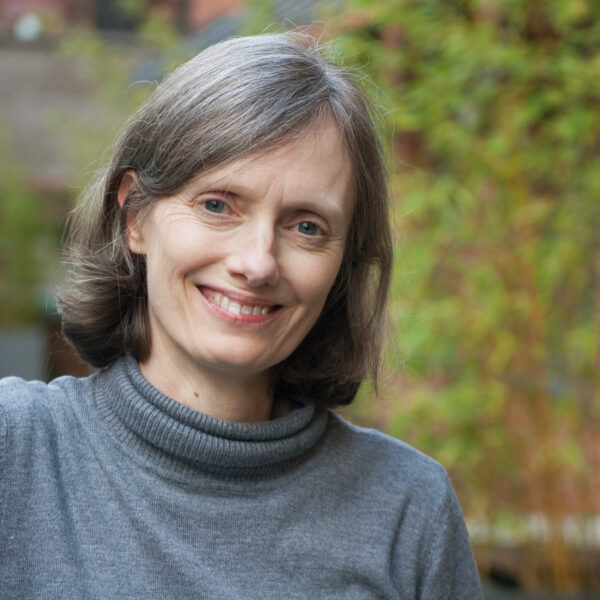 A cheerful woman with gray hair smiles warmly at the camera.