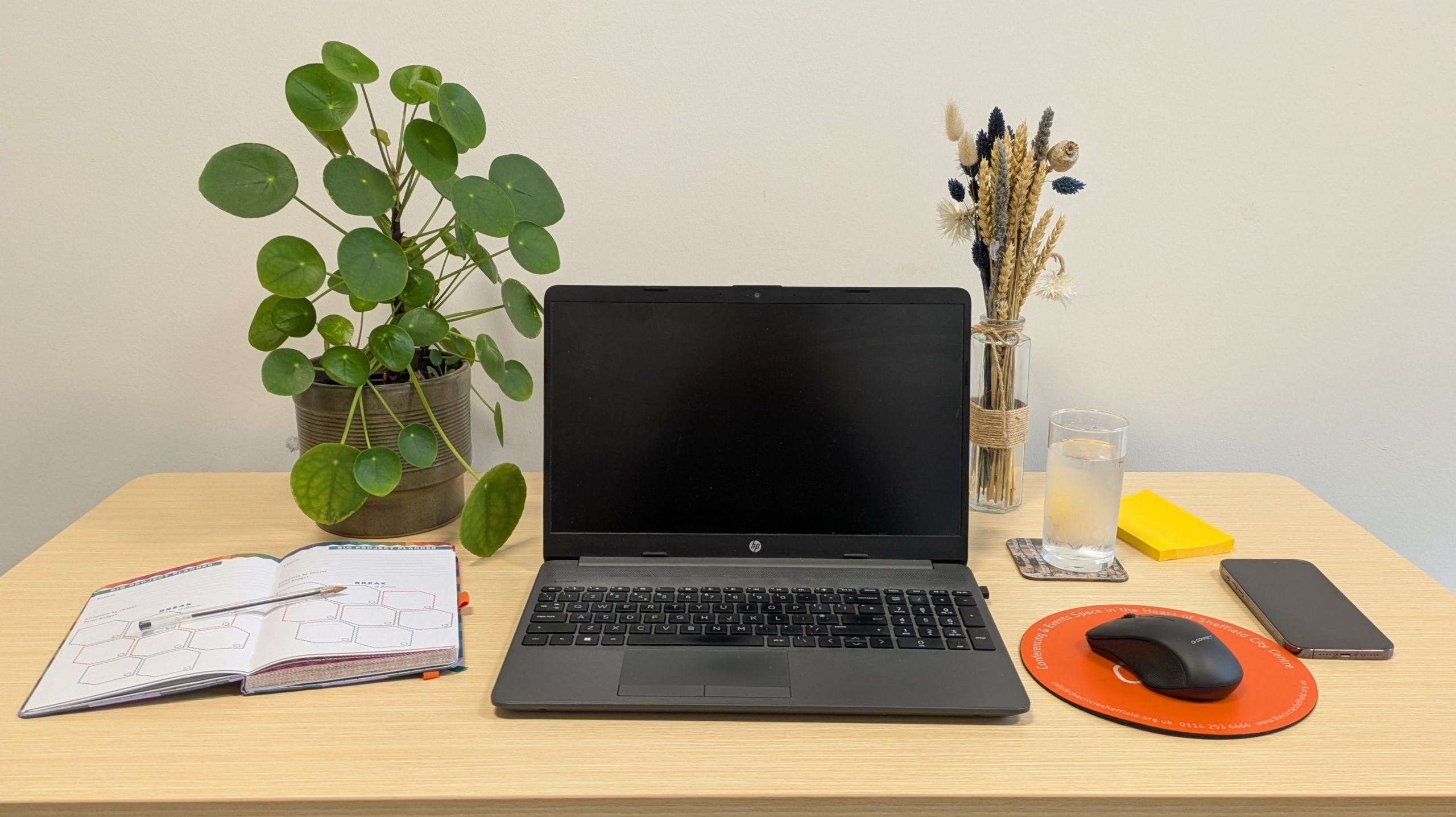 A laptop, mouse, and notebook arranged neatly on a wooden desk, showcasing a workspace setup.