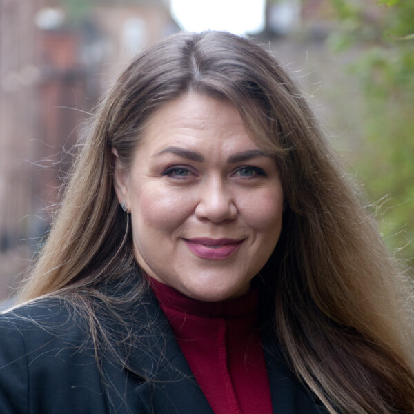 A woman with long hair dressed in a red shirt poses confidently for the photo.