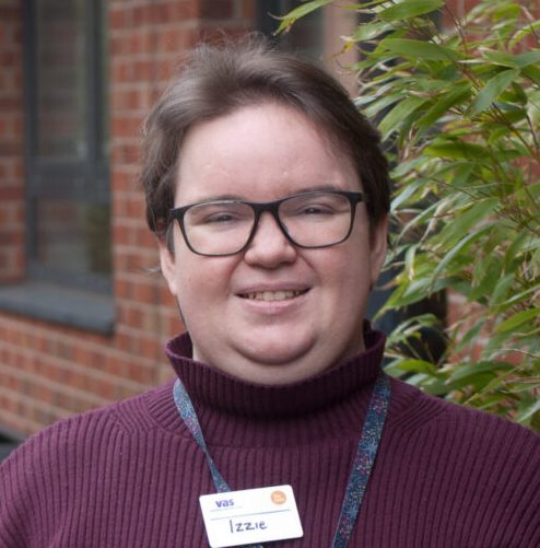 A woman wearing glasses and a purple sweater, seated and gazing directly at the viewer.
