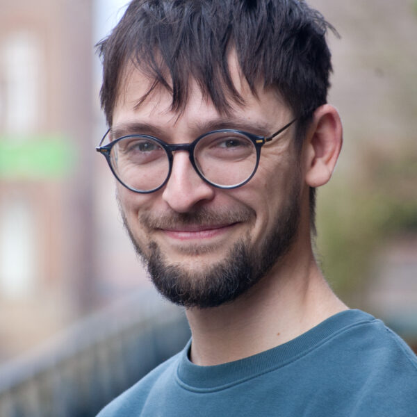 A cheerful man with glasses and a beard smiles for the photo.