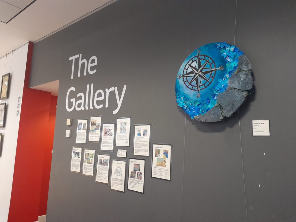The entrance wall to the Gallery with a large, circular, blue art piece that features flowers and a compass.