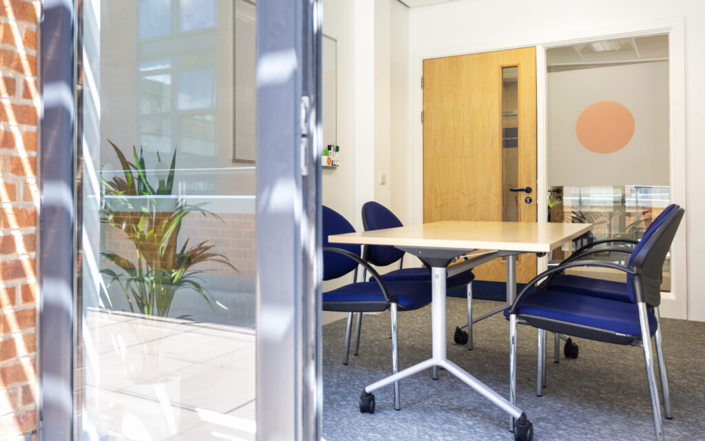 A table with four blue chairs can be seen from a doorway that opens onto the balcony.