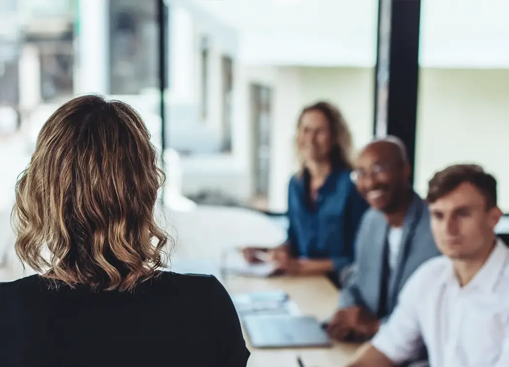 A workshop meeting with four people. A lady has her back to the camera and is teaching the three attendees.